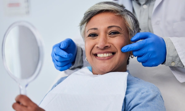 Smiling female dentist in blue gloves giving thumbs up in dental office