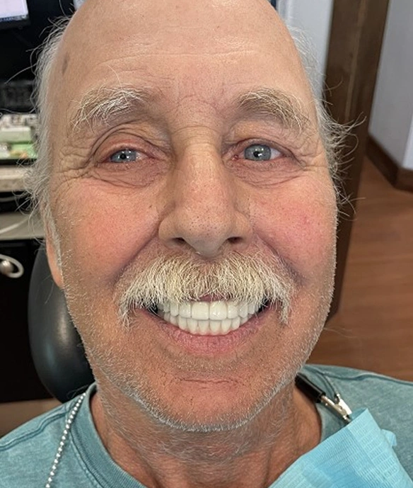 Smiling man with mustache in dental office setting wearing light blue shirt